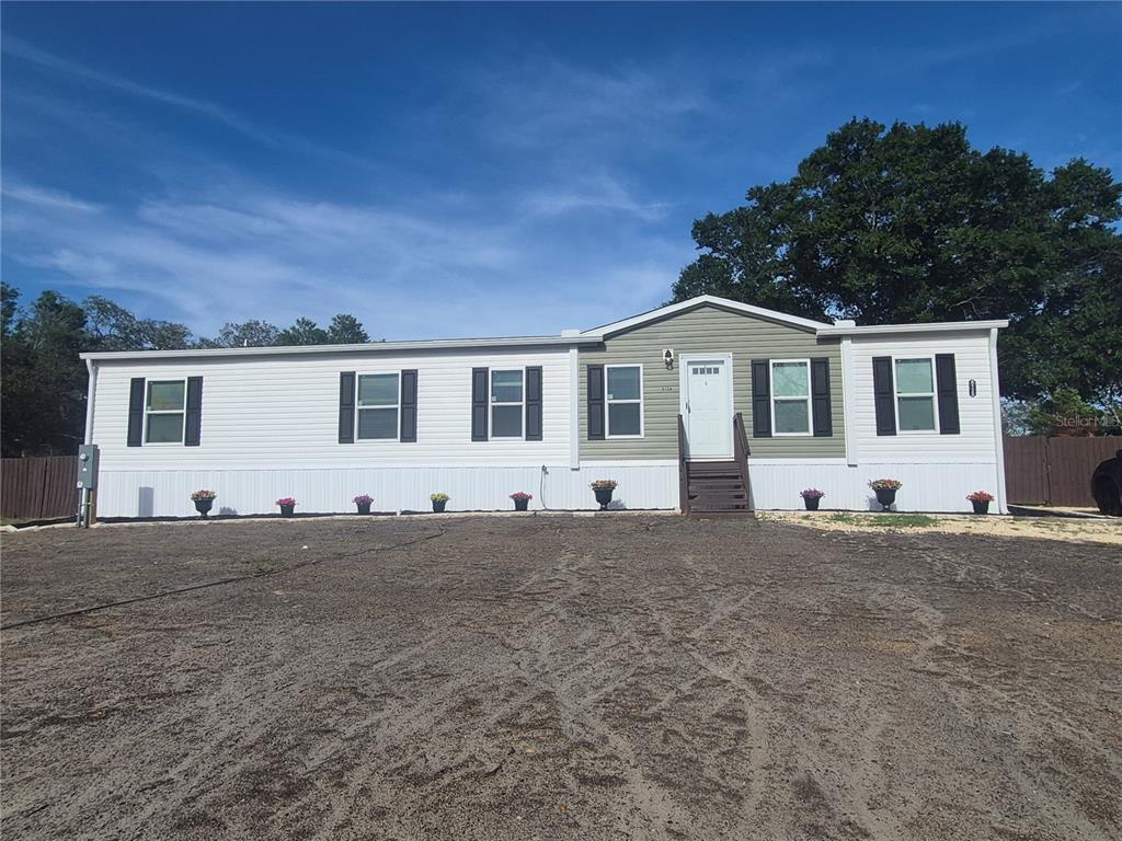 A single-story manufactured home with white and olive siding sits on a dirt lot — 8128 WEEPING WILLOW STREET, BROOKSVILLE, FL