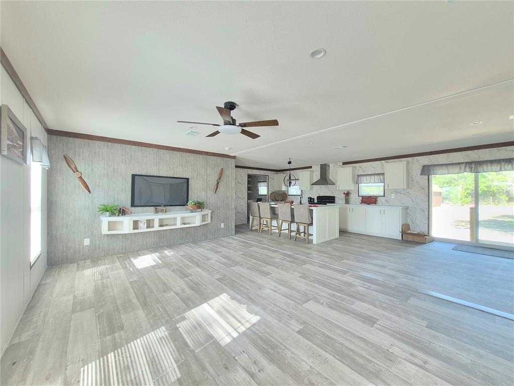 An open-concept living room and kitchen featuring wood-look flooring, a wall-mounted television, and an island — 8128 WEEPING WILLOW STREET, BROOKSVILLE, FL