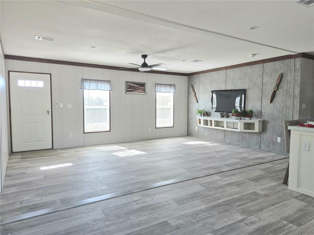 A living room features gray wood-look flooring, a ceiling fan, and a wall-mounted television — 8128 WEEPING WILLOW STREET, BROOKSVILLE, FL