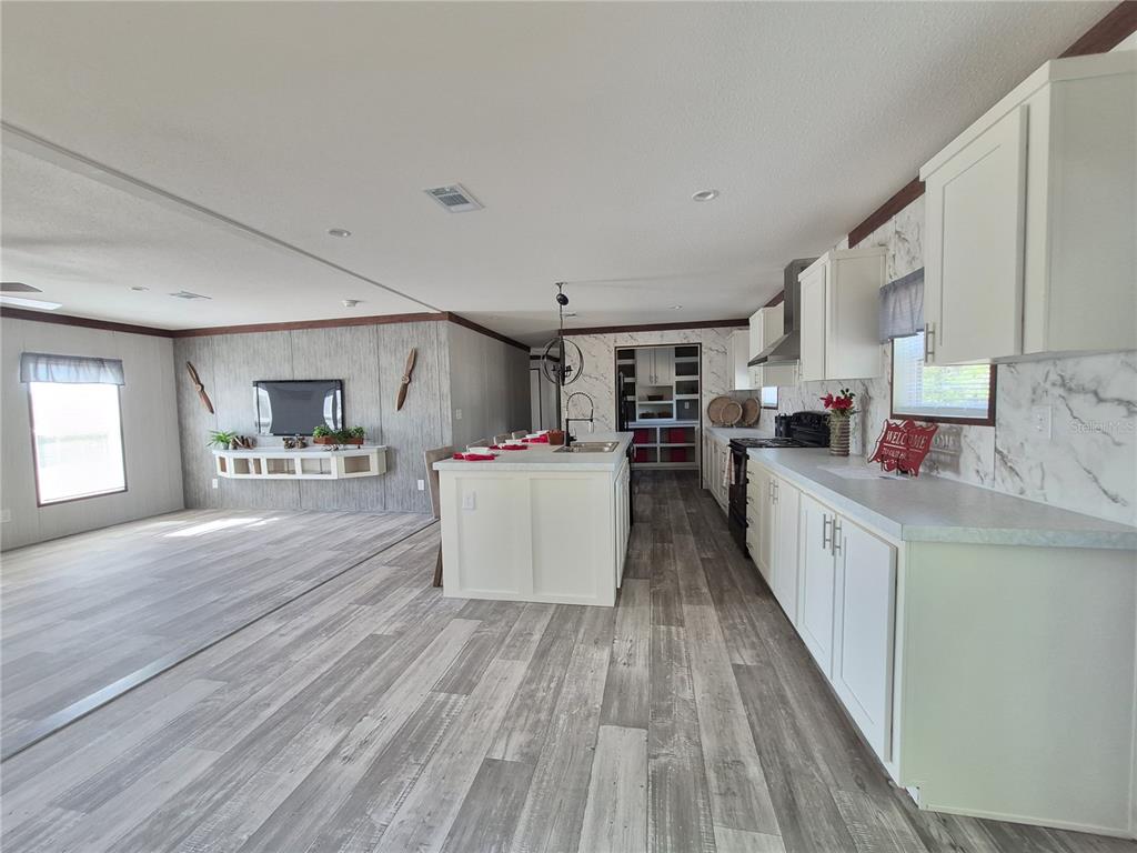 A kitchen with white cabinets and a center island opens into a living area — 8128 WEEPING WILLOW STREET, BROOKSVILLE, FL