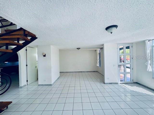 A room with white tile floors, a black metal staircase, and a glass-paneled front door — 70 VIA PLAYERA, TOA BAJA, PR