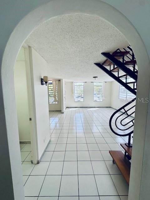 An arched doorway opens into a tiled living area with a black metal staircase — 70 VIA PLAYERA, TOA BAJA, PR