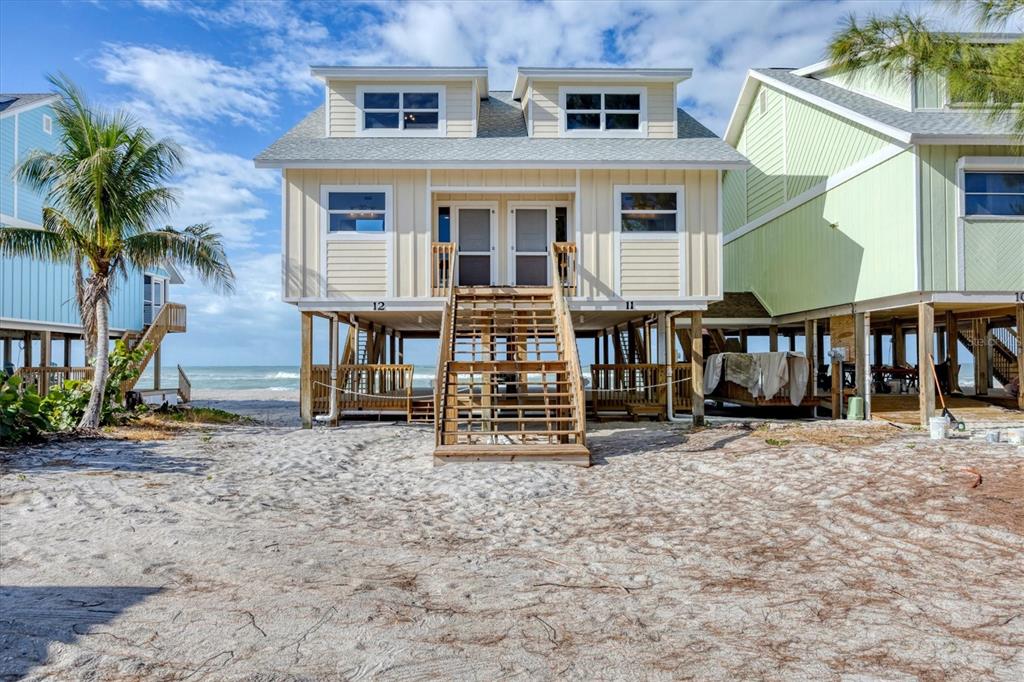 A yellow elevated beach house with a central staircase stands on a sandy lot — 301 S GULF BOULEVARD UNIT 12, PLACIDA, FL