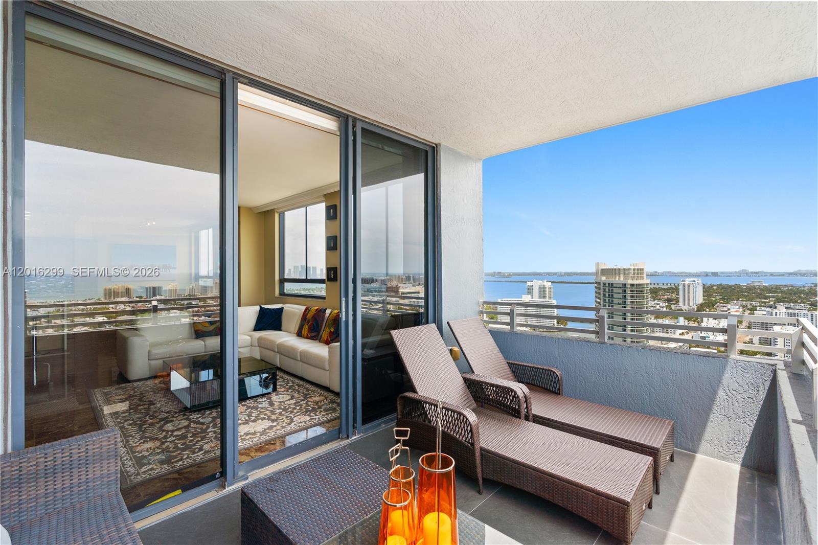 A balcony with two lounge chairs overlooks a city skyline and a large body of water — 1330 West Ave, Miami Beach FL 33139, MIAMI BEACH, FL
