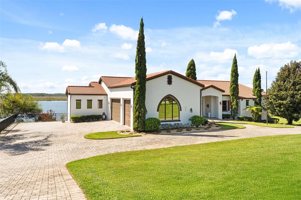 A white house with a tile roof and arched window sits beside a lake — 7616 LILY COURT, GROVELAND, FL