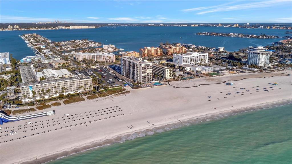An aerial view shows a sandy beach lined with multi-story hotels and residential buildings — 5396 GULF BOULEVARD UNIT 407, ST PETE BEACH, FL