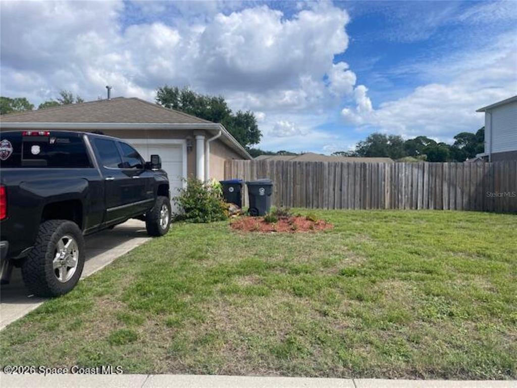 A black pickup truck is parked on a driveway next to a house with a fence — 616 PEACHTREE STREET, TITUSVILLE, FL