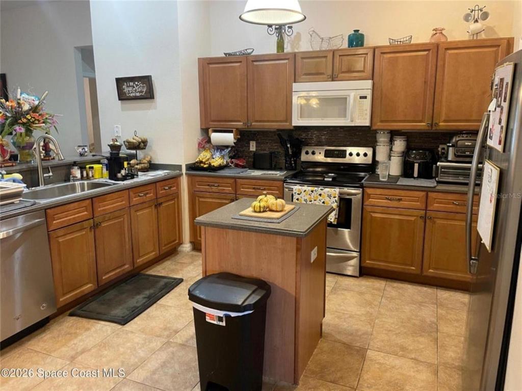 A kitchen features wood cabinets, a central island, stainless steel appliances, and tile flooring — 616 PEACHTREE STREET, TITUSVILLE, FL