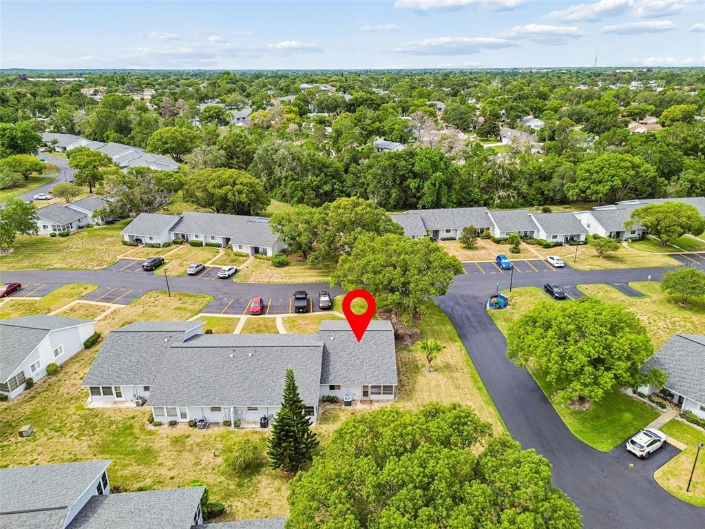 An aerial view shows a residential complex with gray-roofed buildings, parking lots, and surrounding trees — 7725 DANUBE DRIVE UNIT 0000, HUDSON, FL