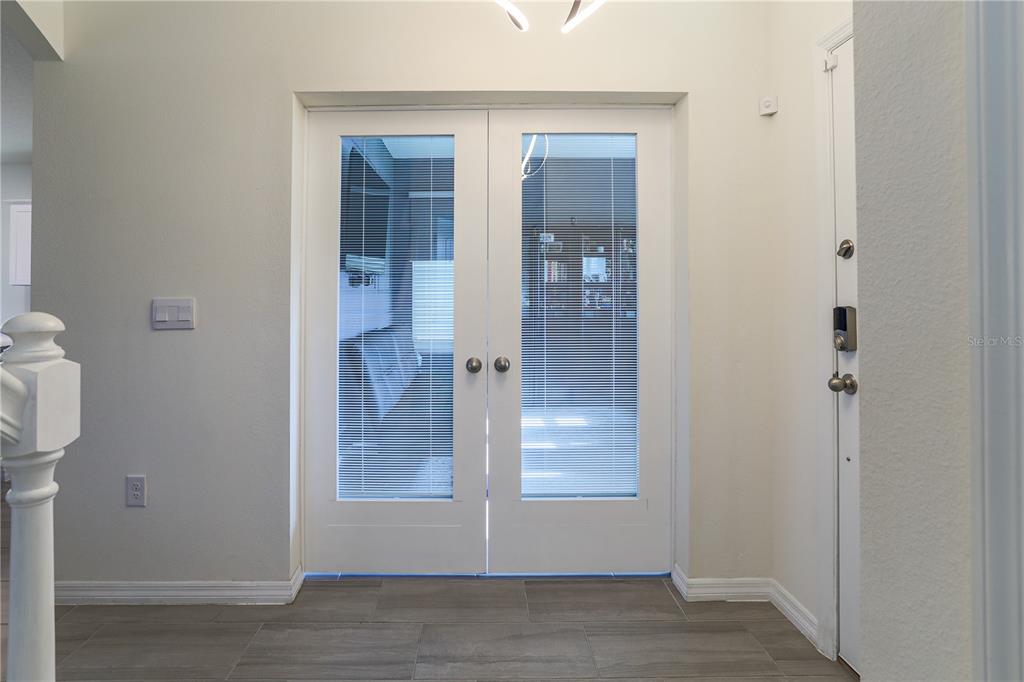 A foyer features double glass-paneled doors with integrated blinds and light-colored tile flooring — 16625 POINT ROCK DRIVE, WINTER GARDEN, FL
