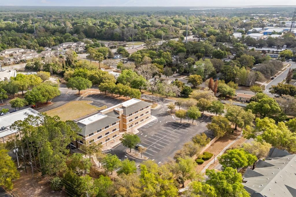An aerial view shows a multi-story commercial building with a parking lot and surrounding trees — 1490 SUNSHADOW DRIVE, CASSELBERRY, FL