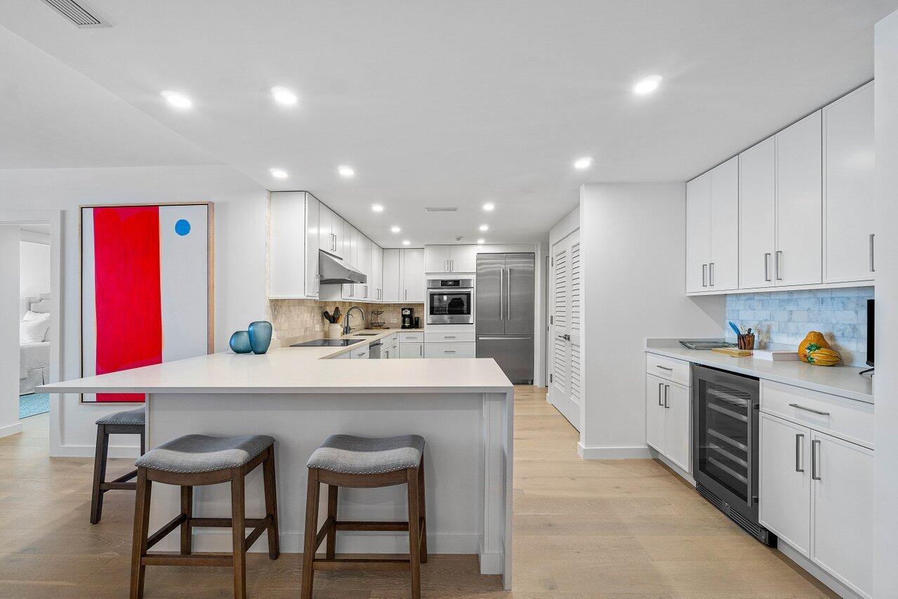 A modern white kitchen features a central island, stainless steel appliances, and light wood flooring — 2784 S Ocean Boulevard # 403s, Palm Beach FL 33480, PALM BEACH, FL