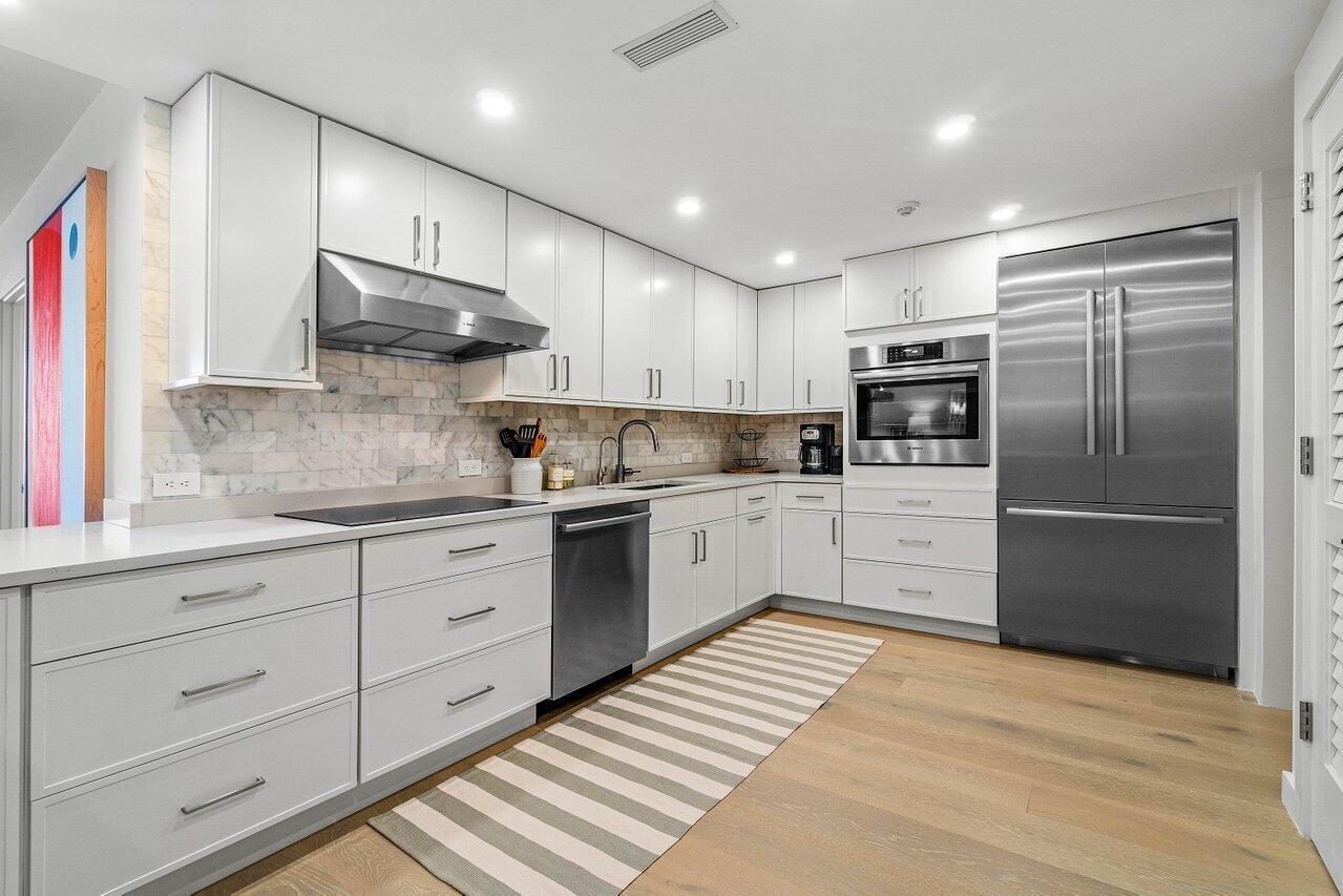 A modern kitchen features white cabinetry, stainless steel appliances, marble backsplash, and light wood flooring — 2784 S Ocean Boulevard # 403s, Palm Beach FL 33480, PALM BEACH, FL
