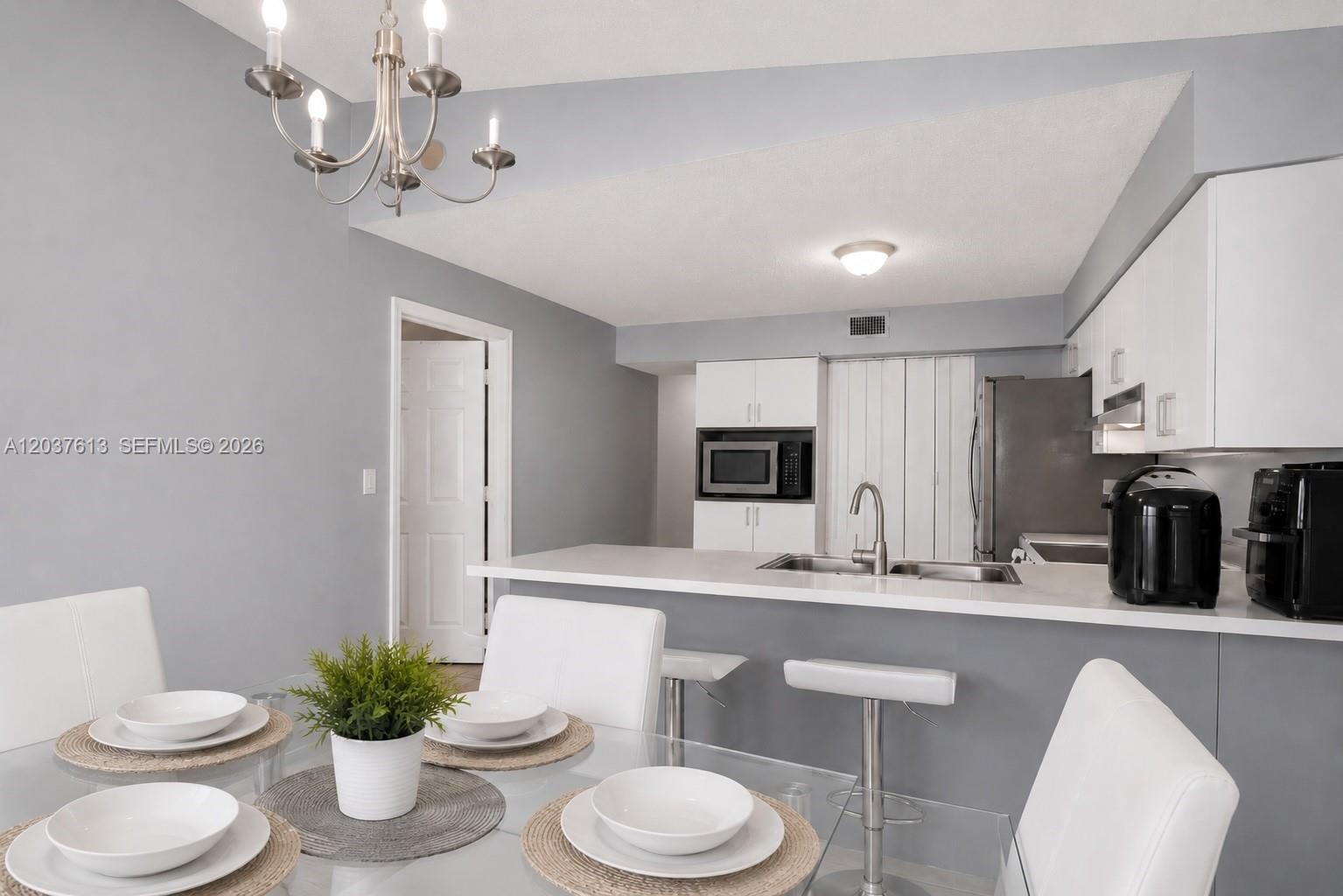 A dining area with a glass table sits adjacent to a kitchen with white cabinets — 2886 W 74th Pl, Hialeah FL 33018, HIALEAH, FL