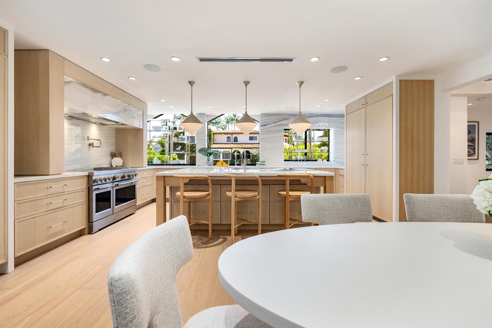 A modern kitchen features light wood cabinetry, a large island, and marble backsplashes — 260 Everglade Avenue, Palm Beach FL 33480, PALM BEACH, FL