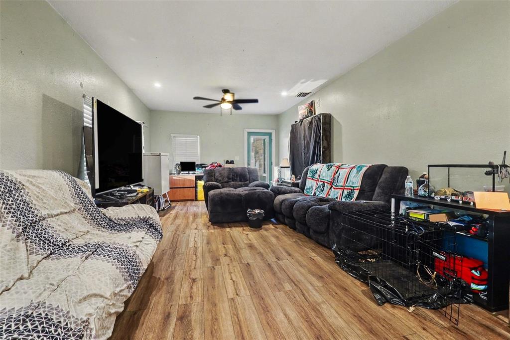 A living room with wood-look flooring, a ceiling fan, a large television, and dark furniture — 1054 STATE ROAD 60 E, LAKE WALES, FL