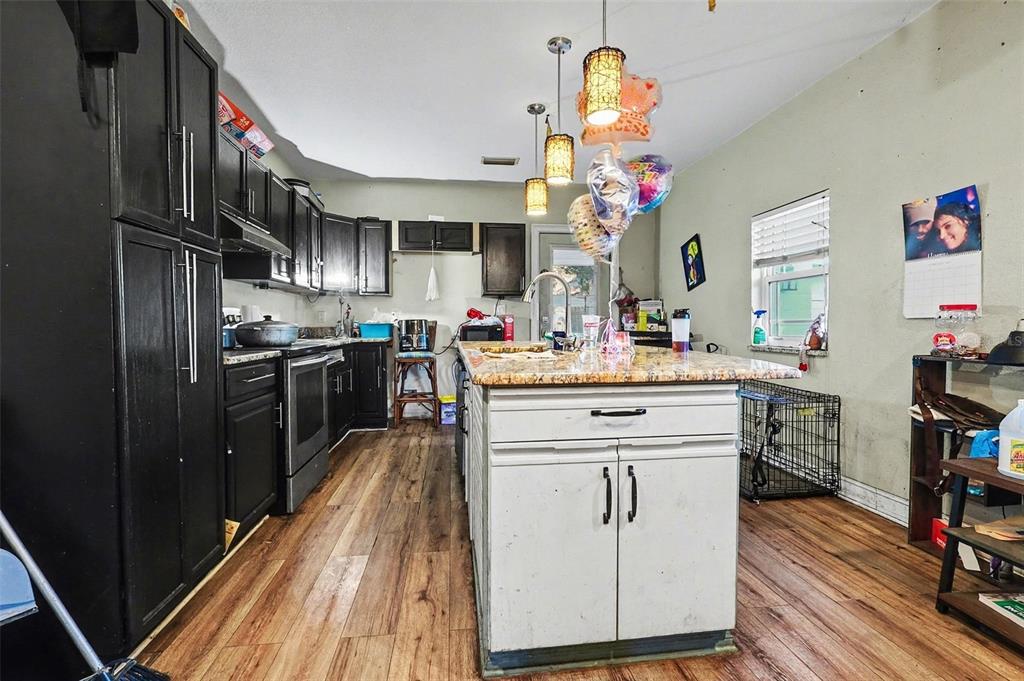 A kitchen features dark cabinets, a white center island with a granite countertop, and wood-look flooring — 1054 STATE ROAD 60 E, LAKE WALES, FL