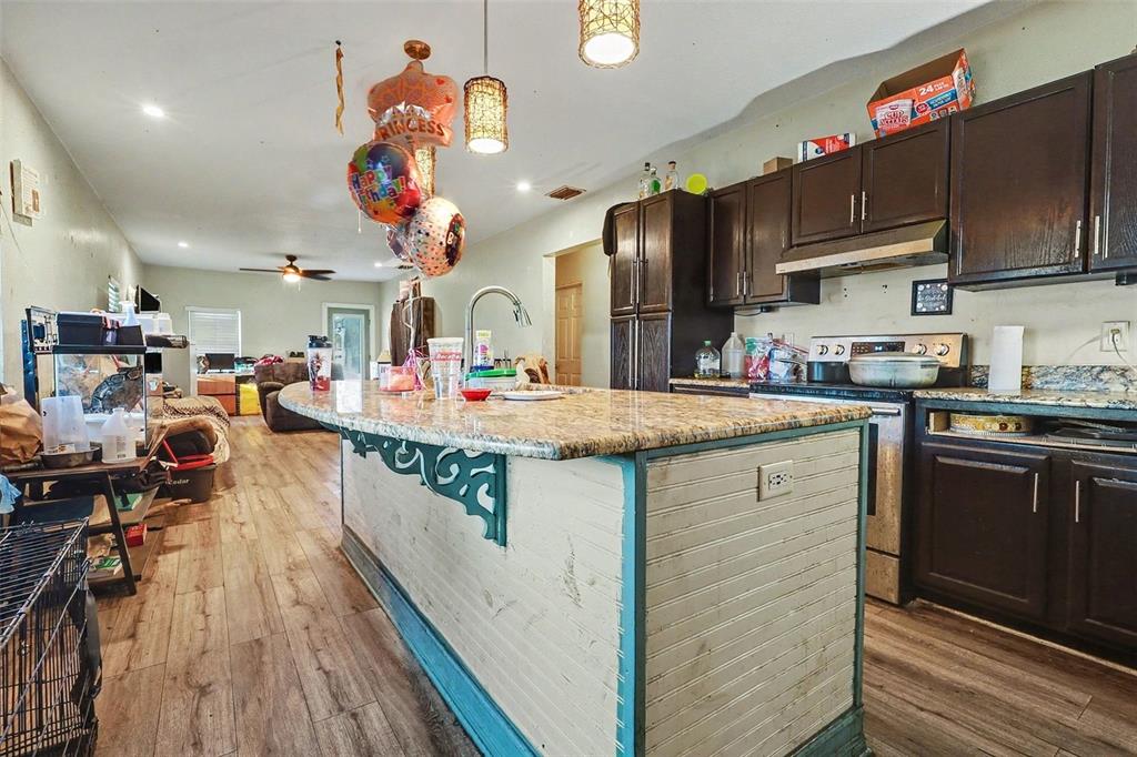 A kitchen features a granite-topped island with beadboard paneling, dark wood cabinets, and wood flooring — 1054 STATE ROAD 60 E, LAKE WALES, FL