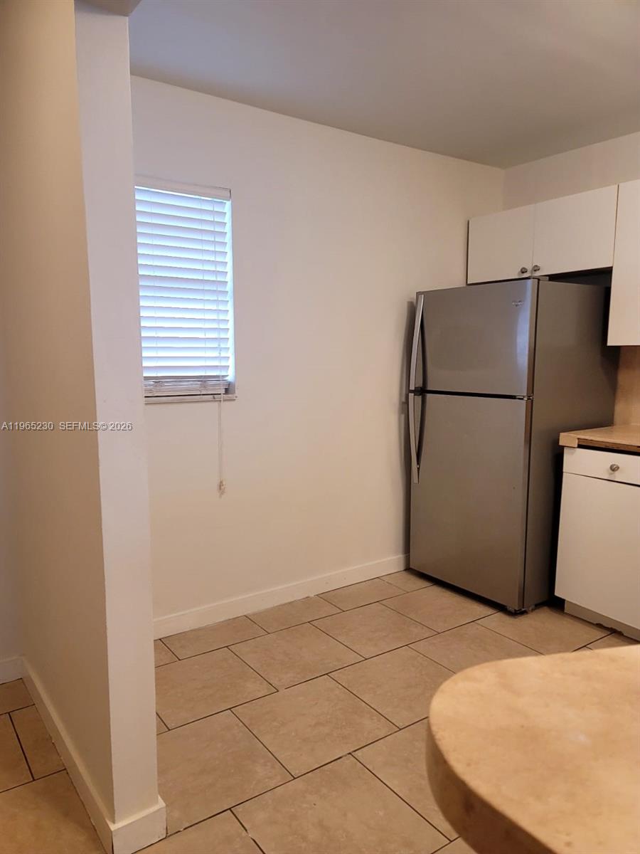A kitchen features a stainless steel refrigerator, white cabinets, and light-colored tile flooring — 1690 NE 191st St # 1, Miami FL 33179, MIAMI, FL