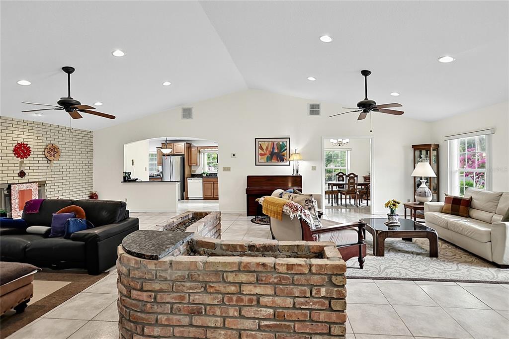 A spacious living room features a brick fireplace, tile flooring, and a vaulted ceiling — 550 ARAPAHO TRAIL, MAITLAND, FL