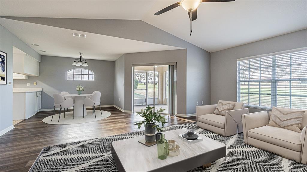 A living room and dining area with vaulted ceilings, wood-look flooring, and sliding glass doors — 11048 MOSHIE LANE, SAN ANTONIO, FL