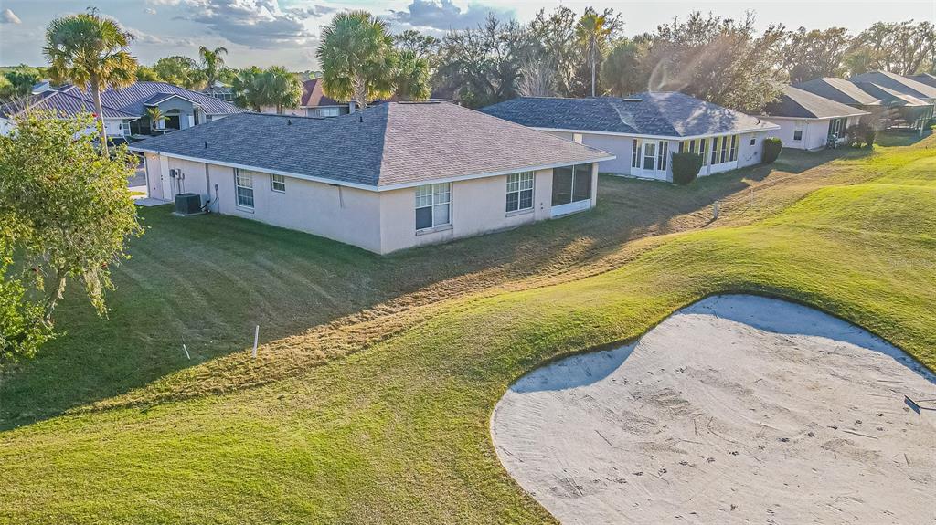 A screened-in patio overlooks a golf course with a sand bunker and distant houses — 11048 MOSHIE LANE, SAN ANTONIO, FL