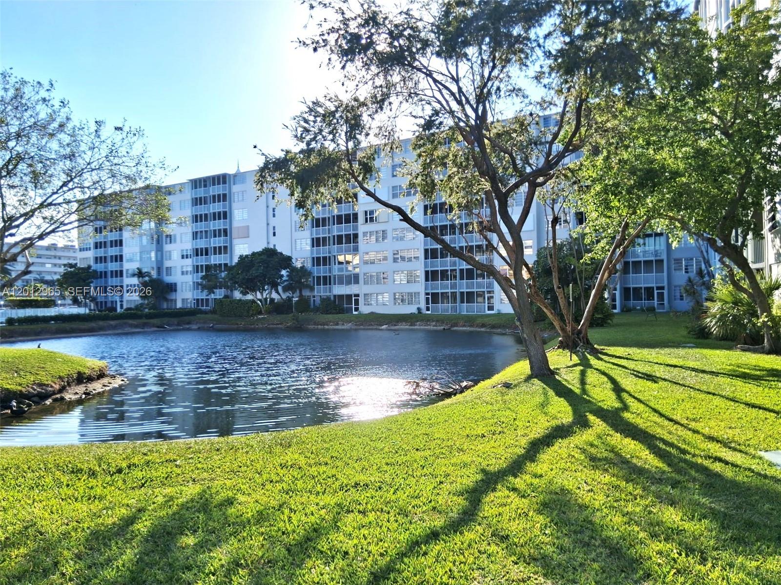 A multi-story apartment building overlooks a pond surrounded by green lawns and trees — 1770 NE 191st St # 1, Miami FL 33179, MIAMI, FL