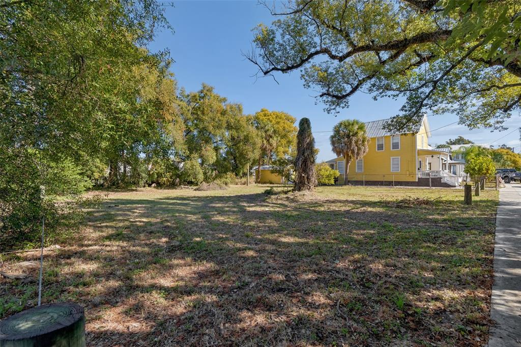 A vacant grassy lot sits next to a two-story yellow house under a clear sky — 1012 E 12TH AVENUE UNIT 2, TAMPA, FL