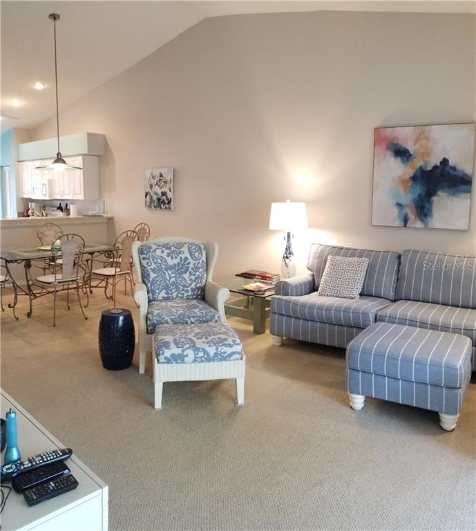 A living room with a striped sofa, a patterned armchair with ottoman, and an adjacent dining area — 8951 VERANDA WAY UNIT 625, SARASOTA, FL
