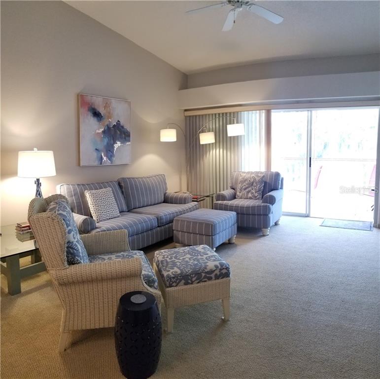 A living room features a striped sofa, matching armchair, wicker chair, and sliding glass doors — 8951 VERANDA WAY UNIT 625, SARASOTA, FL