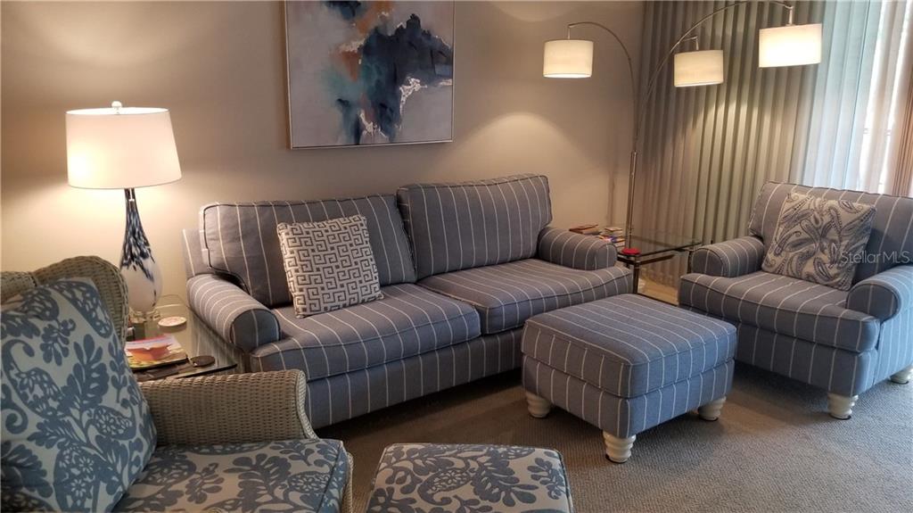 A living room features a striped sofa, matching ottoman, armchair, and a floor lamp — 8951 VERANDA WAY UNIT 625, SARASOTA, FL