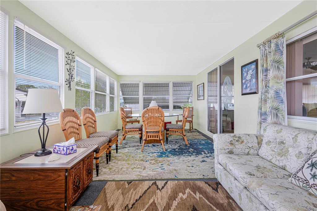 A sunroom features a dining set, wicker chairs, a sofa, and large windows with blinds — 3324 TIKI DRIVE, HOLIDAY, FL