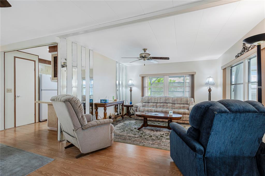 A living room features wood flooring, a mirrored wall, a ceiling fan, and upholstered furniture — 3324 TIKI DRIVE, HOLIDAY, FL