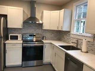 A kitchen features white cabinets, stainless steel appliances, a tiled backsplash, and light countertops — 1741 NW 6TH AVENUE, GAINESVILLE, FL