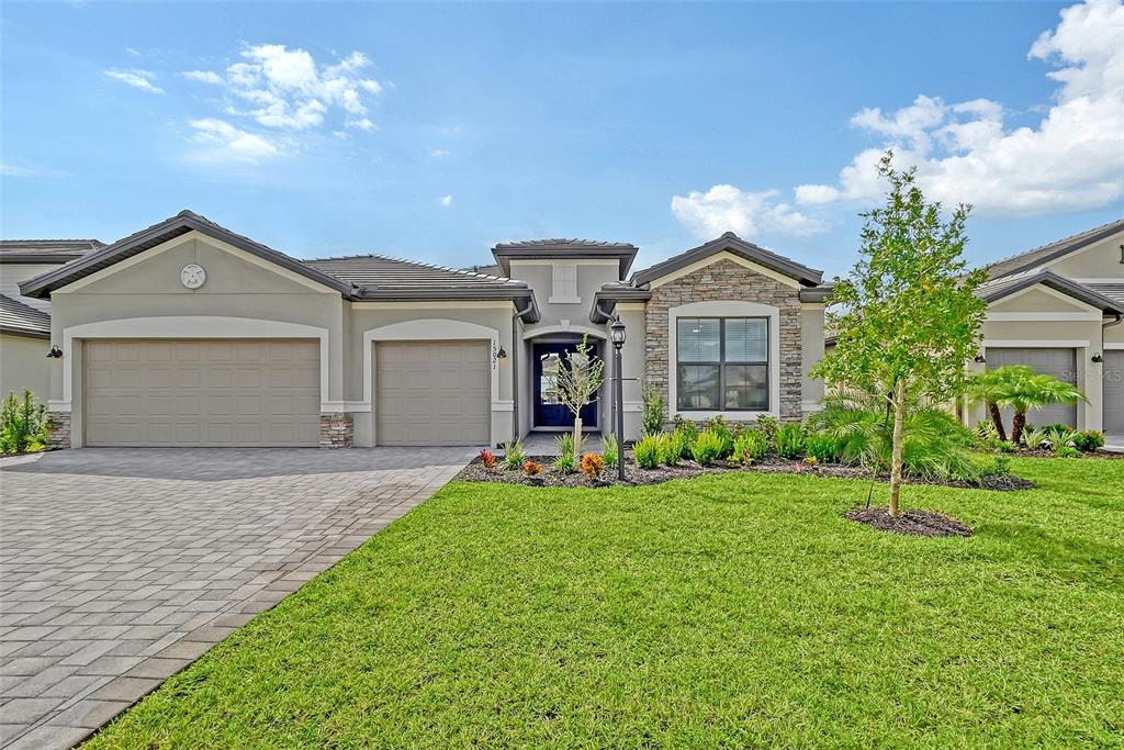 A single-story house with a paved driveway, three-car garage, and stone-accented exterior facade — 15021 SEA SALT WAY, BRADENTON, FL