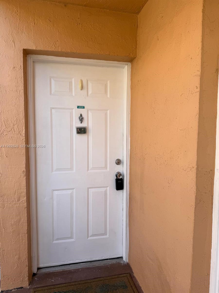 A white front door with a unit number and lockbox is set in a peach-colored wall — 14907 SW 80th St # 205, Miami FL 33193, MIAMI, FL