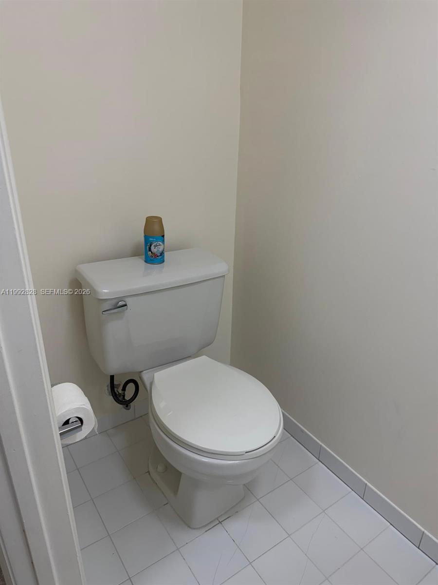 A white toilet sits in a small bathroom with white tiled flooring and plain walls — 14907 SW 80th St # 205, Miami FL 33193, MIAMI, FL