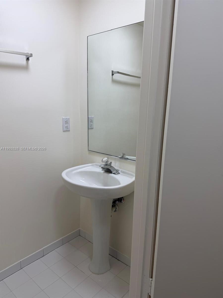 A small bathroom features a white pedestal sink, a wall-mounted mirror, and tiled flooring — 14907 SW 80th St # 205, Miami FL 33193, MIAMI, FL
