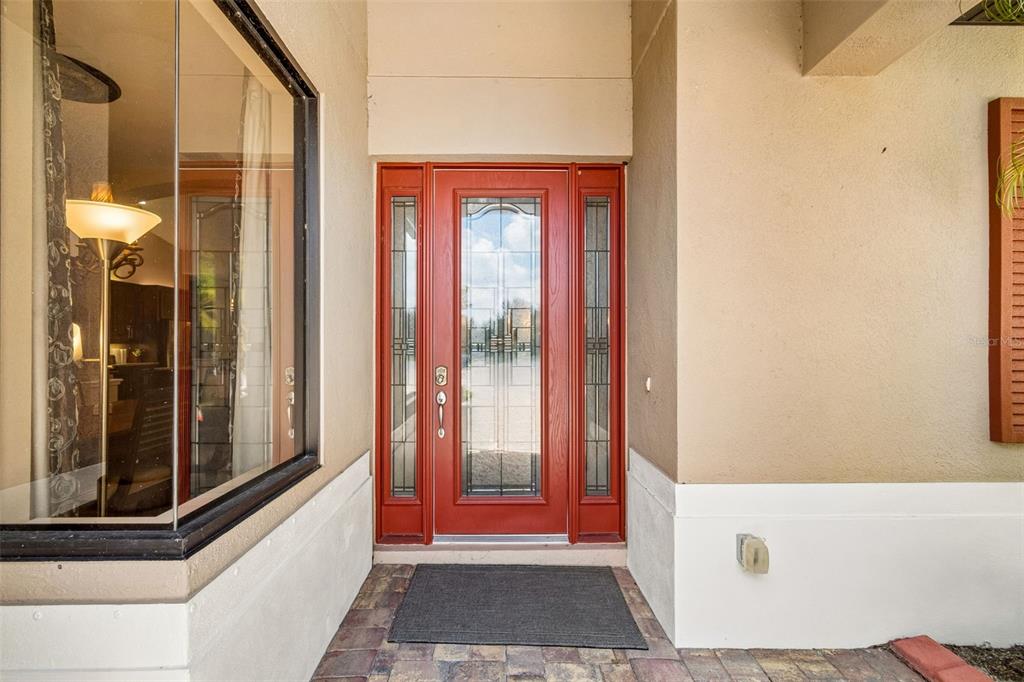 A red front door with glass panels sits in a covered entryway with a doormat — 5919 118TH TERRACE E, PARRISH, FL
