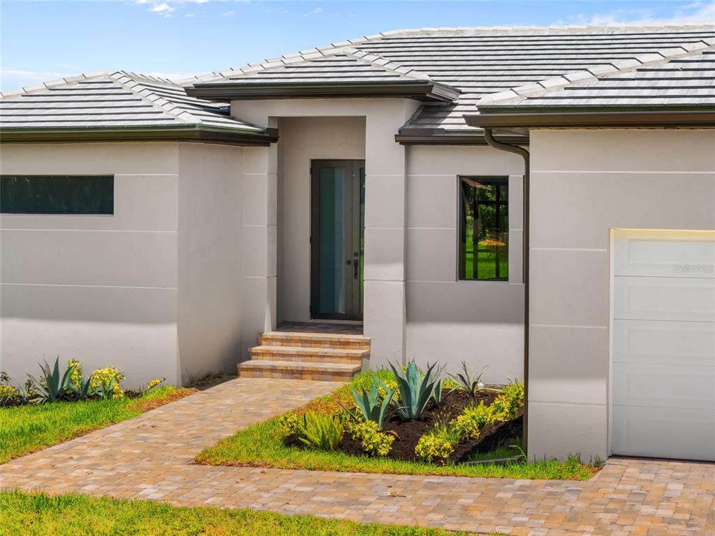 A modern house exterior features a paved walkway leading to a recessed front entrance — 17200 MINT LANE, PUNTA GORDA, FL