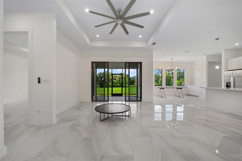 A bright, open-concept living area features white marble-look tile floors, a tray ceiling, and sliding doors — 17200 MINT LANE, PUNTA GORDA, FL