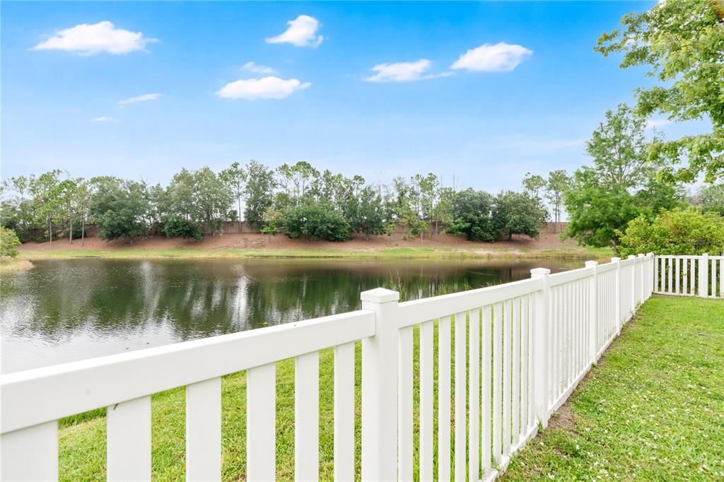 A white vinyl fence borders a grassy backyard overlooking a pond and treeline — 15031 SKIP JACK LOOP, LAKEWOOD RANCH, FL