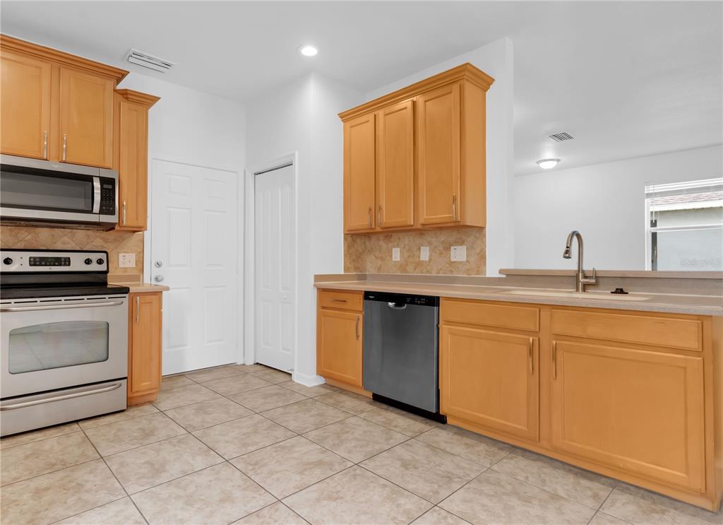 A kitchen features light wood cabinets, stainless steel appliances, and beige tile flooring — 15031 SKIP JACK LOOP, LAKEWOOD RANCH, FL