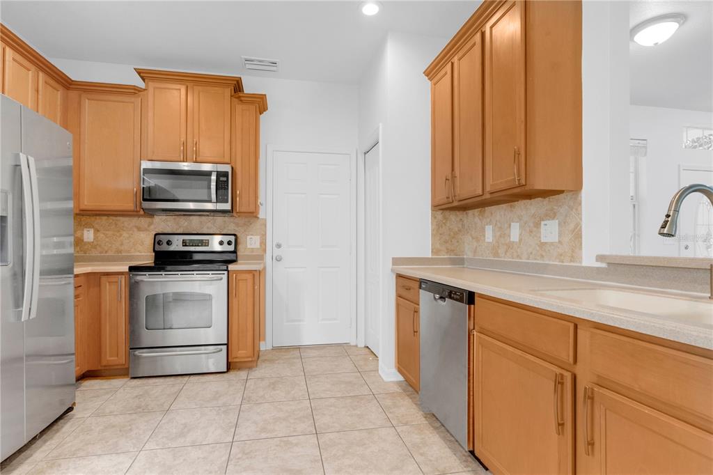 A kitchen features light wood cabinets, stainless steel appliances, tile flooring, and beige countertops — 15031 SKIP JACK LOOP, LAKEWOOD RANCH, FL
