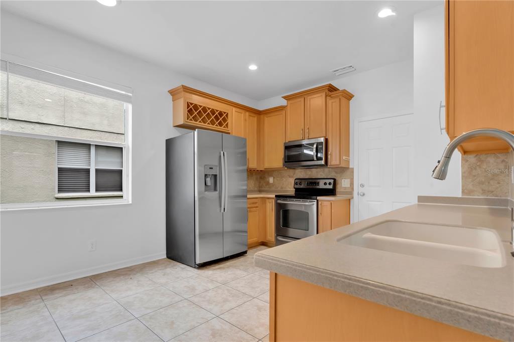 A kitchen features light wood cabinets, stainless steel appliances, a tile floor, and a window — 15031 SKIP JACK LOOP, LAKEWOOD RANCH, FL