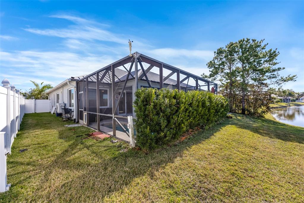 A house exterior features a screened-in pool enclosure, a tall hedge, and a grassy yard — 102 SALAZAR LANE, SEBASTIAN, FL