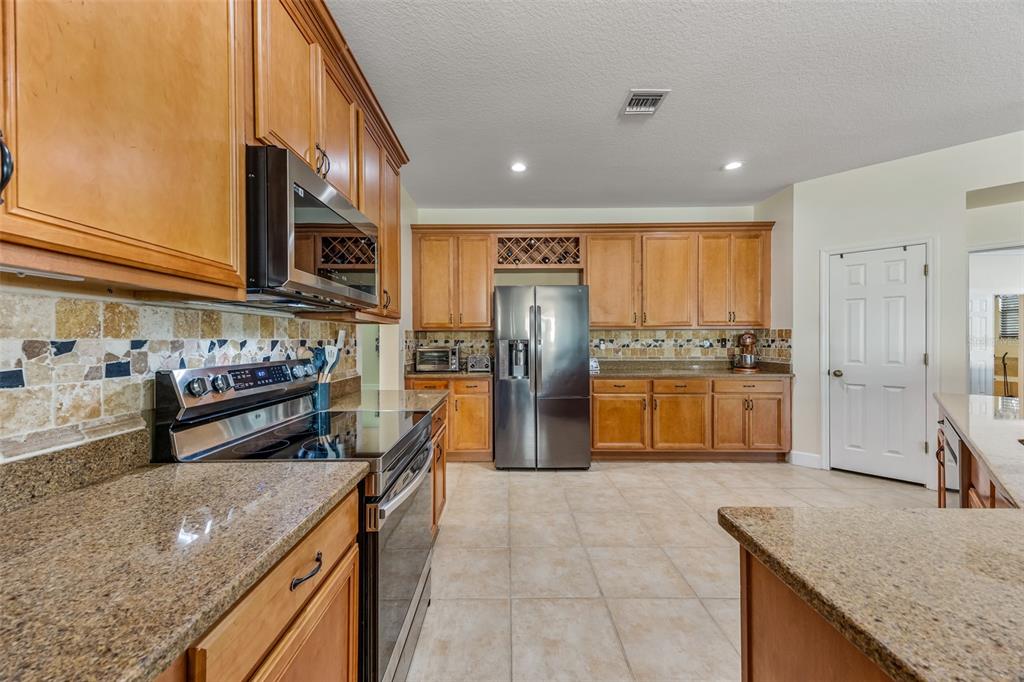 A kitchen features wood cabinets, granite countertops, stainless steel appliances, and a tiled backsplash — 102 SALAZAR LANE, SEBASTIAN, FL