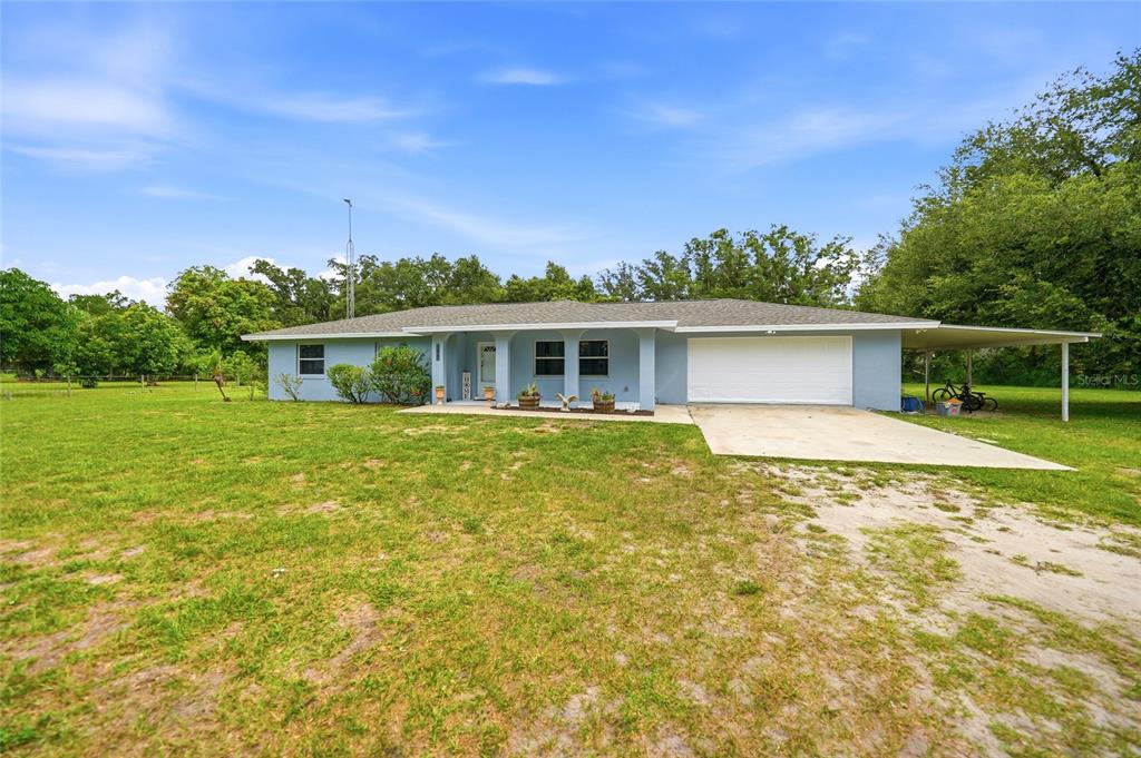 A light blue, single-story ranch-style house with a white garage door and a carport — 2798 SE LOVEJOY STREET, ARCADIA, FL