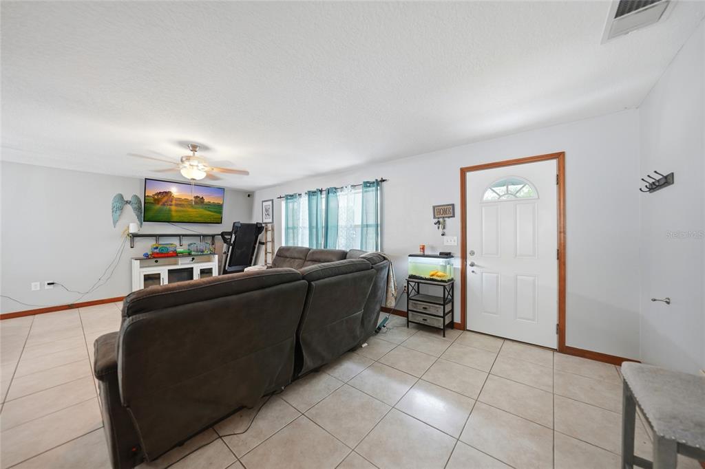 A living room features light-colored tile flooring, a gray sectional sofa, and a wall-mounted television — 2798 SE LOVEJOY STREET, ARCADIA, FL