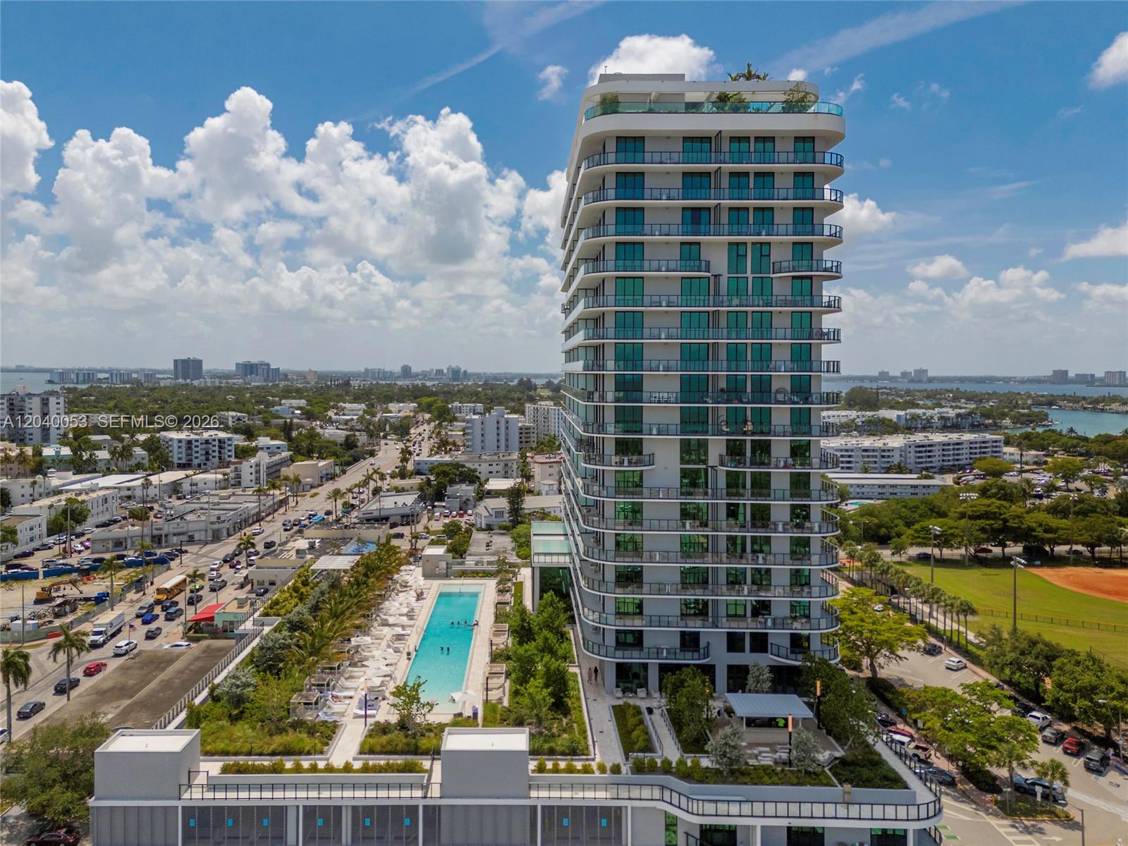 An aerial view shows a modern high-rise apartment building with a swimming pool and deck — 580 72nd St # 1008, Miami Beach FL 33141, MIAMI BEACH, FL